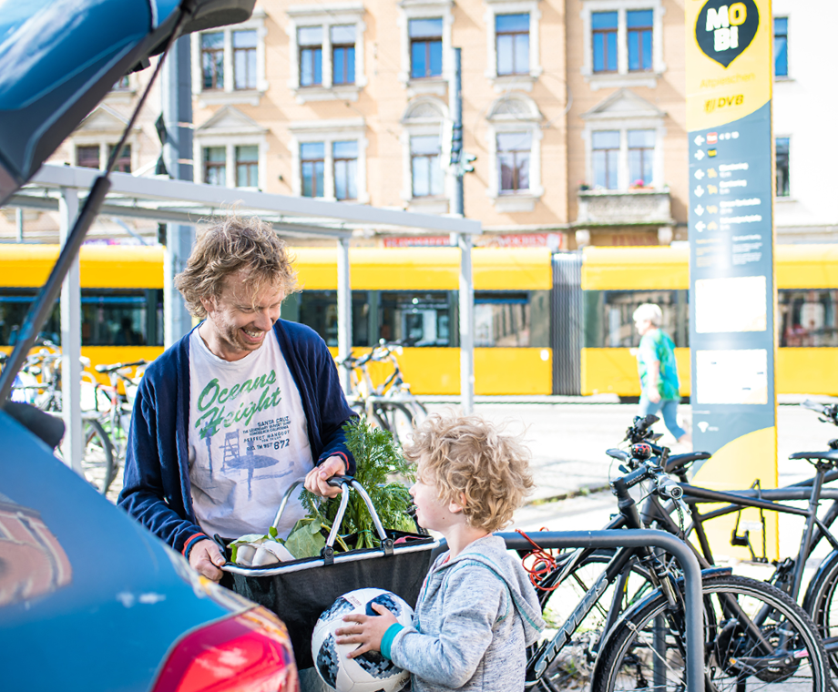 Ein Vater mit seinem Sohn an einem Mobipunkt, sie laden Einkäufe in den Kofferraum